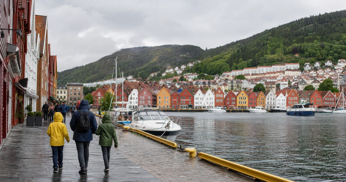 En familie i regnjakker langs en brygge med fargerike trehus i Bergen