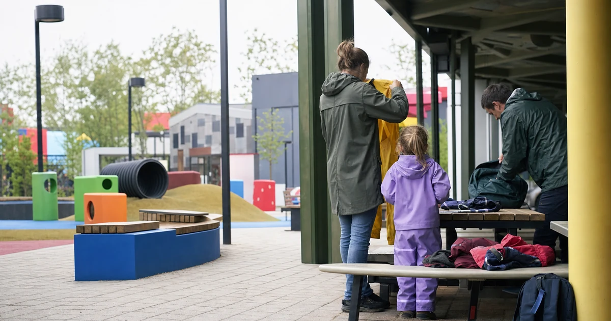 En familie som pakker regntøy ved nøytrale, fargerike lekestrukturer i Billund