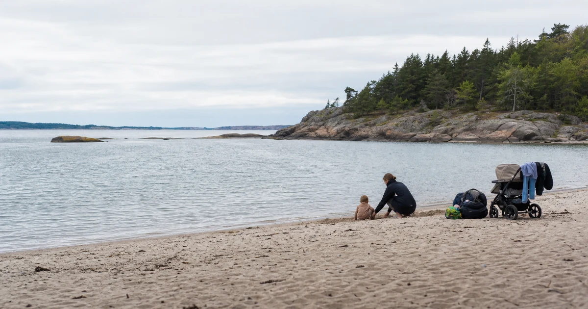 En familie ved en sandstrand på Sørlandet, med barnevogn og bagasje ved siden av