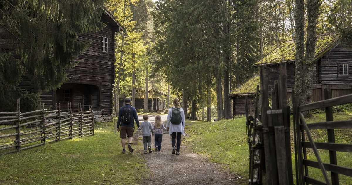 En familie på en skogsti i Lillehammer-området, med trebygninger i bakgrunnen