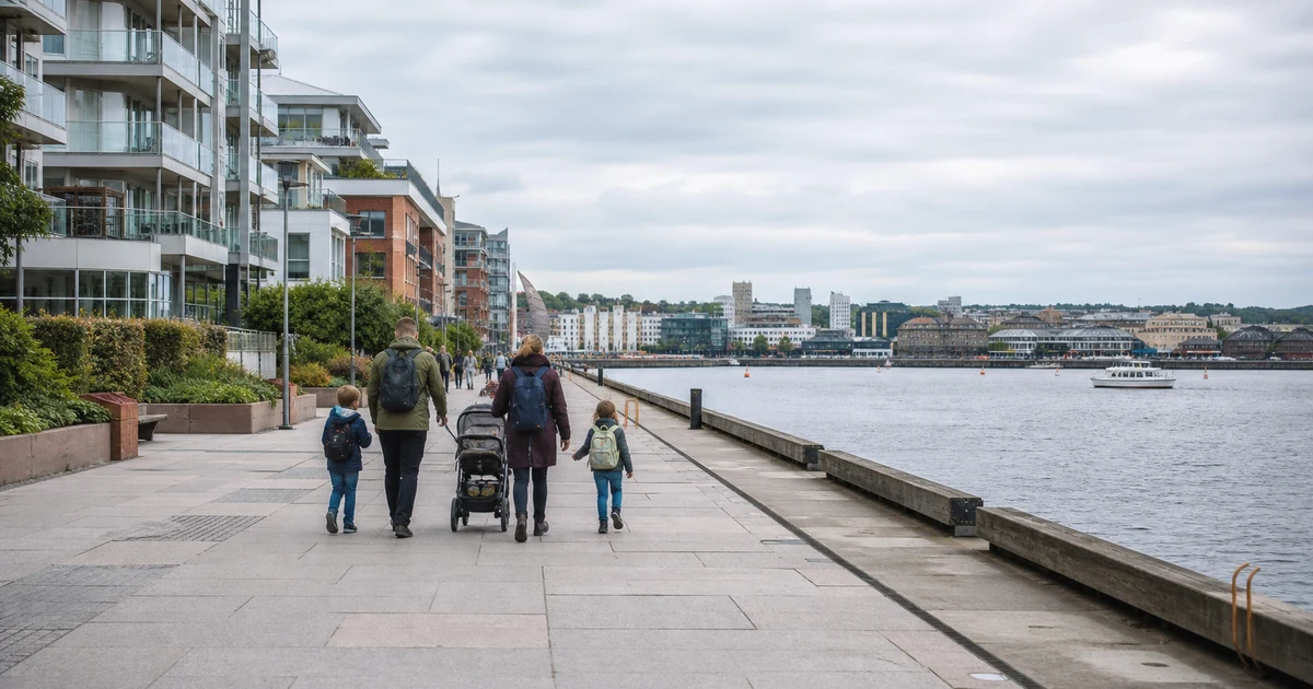 En familie på en bred promenade langs vannet i Oslo, med bybebyggelse i bakgrunnen